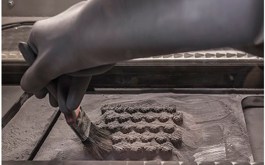 La poudre de métal est brossée loin d'un lit de pièces d'aluminium complexes.